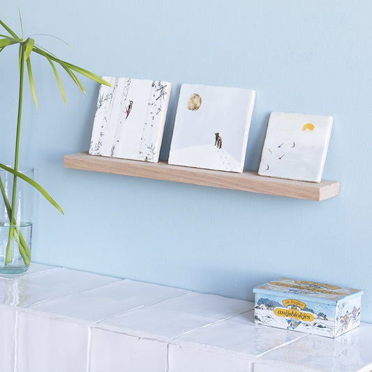 Wandplankje met drie decoratieve tegels tegen blauwe muur