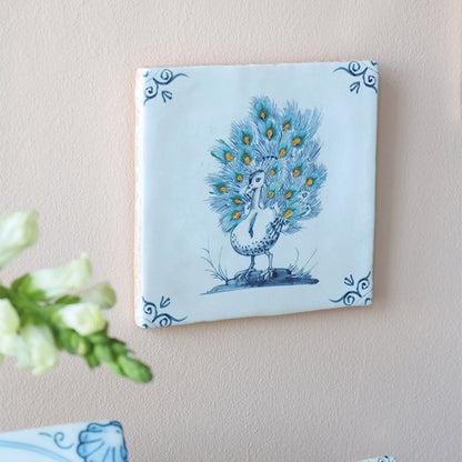 Tegeltje met pauw in blauwe decoratie aan muur bevestigd