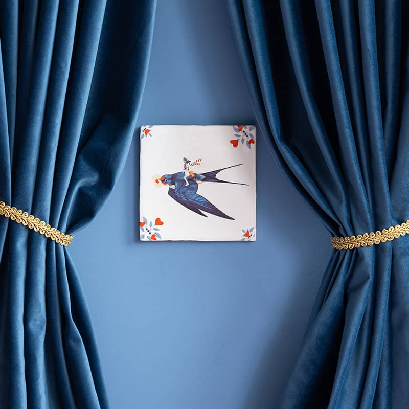 Gepersonaliseerd tegeltje met zwaluw, tussen blauwe gordijnen geplaatst