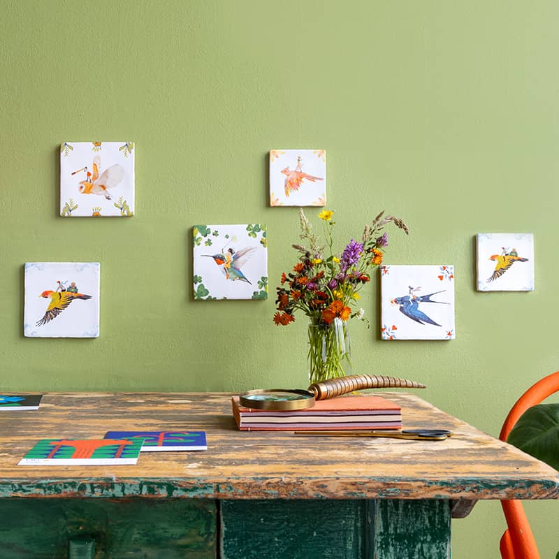 Tegeltjes met vogels aan groene muur boven houten tafel