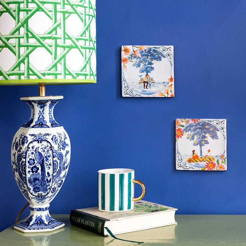 Delfts blauw tegeltje met boom en figuren aan blauwe muur